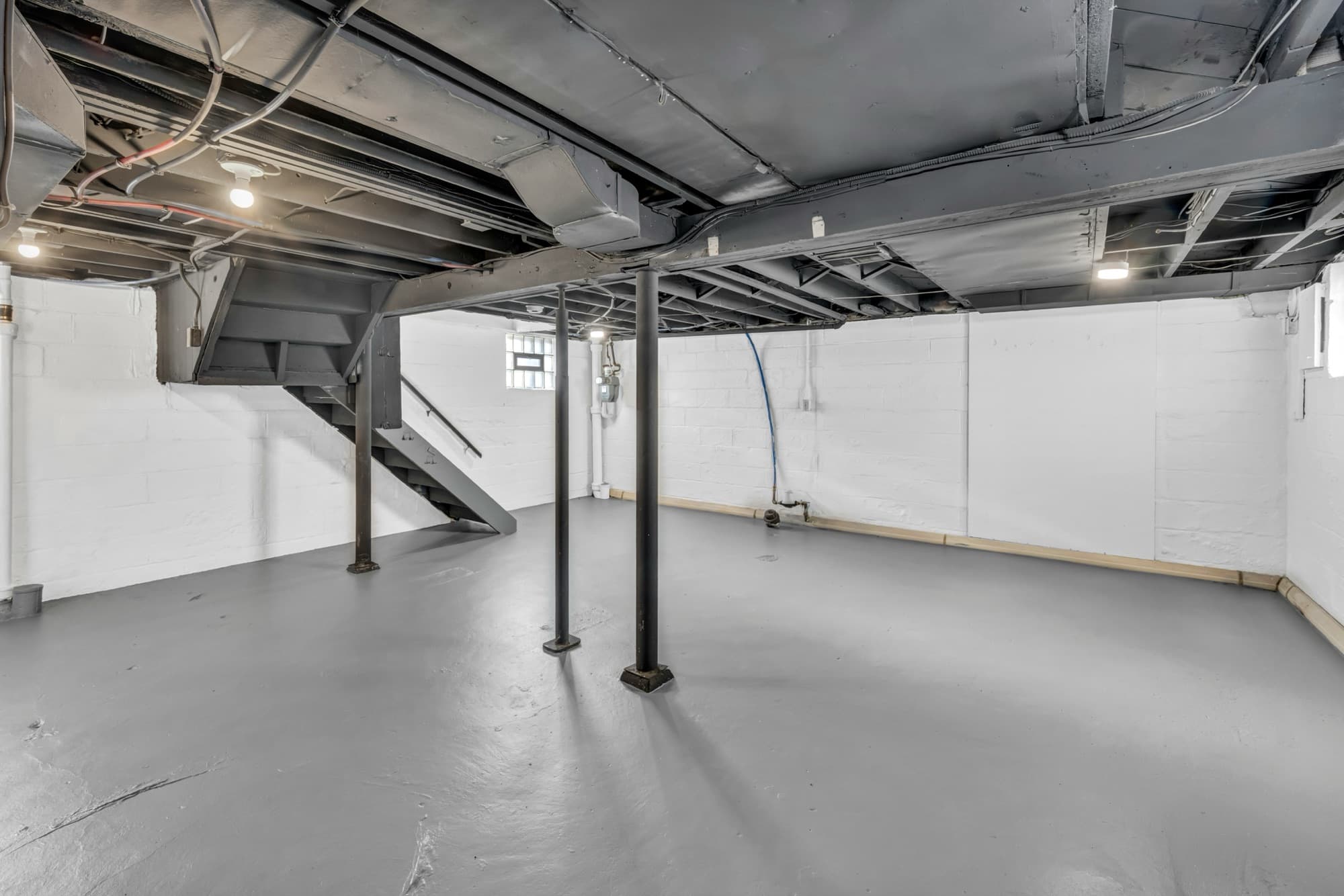 A clean, dry unfinished basement with painted block walls and steel support posts